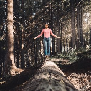 woman in blue denim jeans standing on brown tree log during daytime